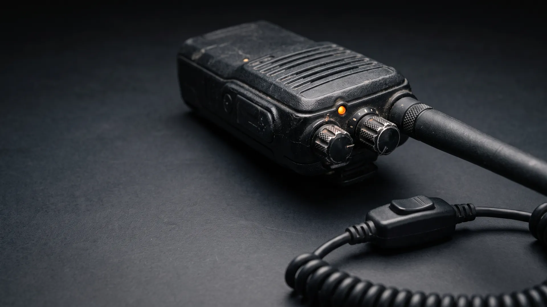 Illustrative radio and coiled push-to-talk cable on a dark workbench